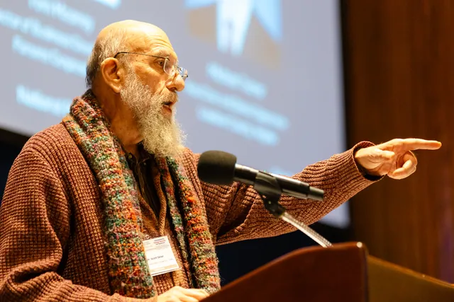 Audience member in a patterned scarf points emphatically while speaking at a microphone.