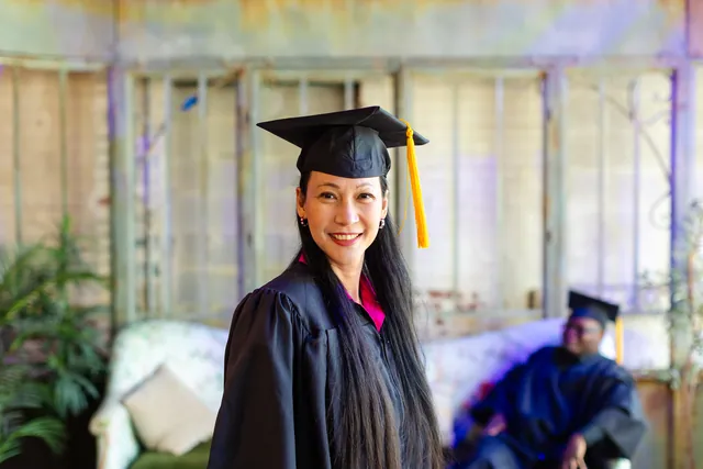 A smiling graduate in a cap with a gold tassel looks into the camera in a bright lounge space.