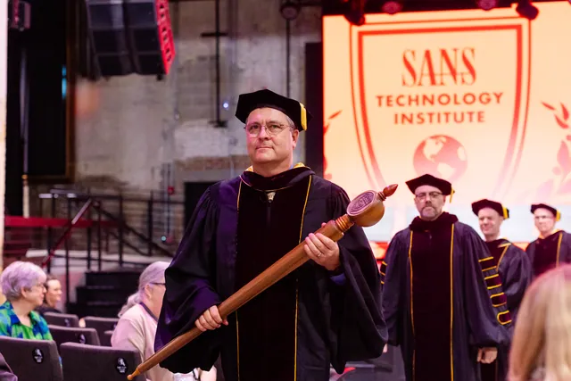 A faculty member carries the ceremonial mace in a processional with a glowing institute logo behind.