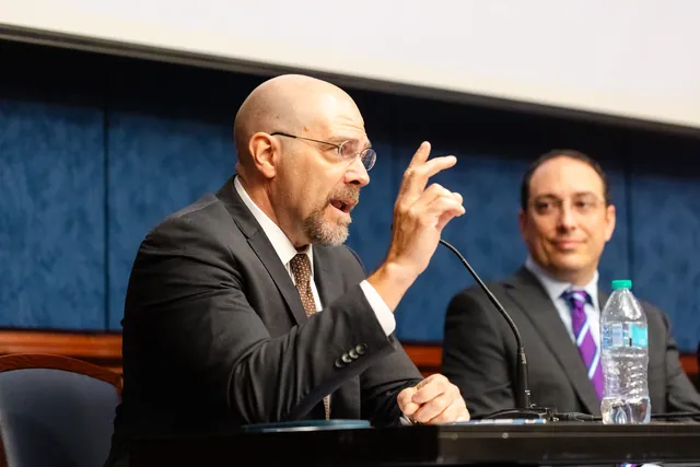 A panelist raises a hand to make a point while another panelist listens beside them.