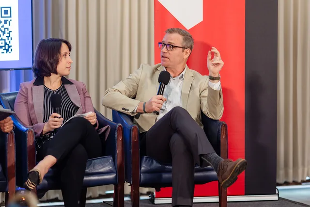 Panelist gesturing with mic against the red banner.