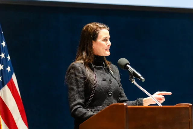Symposium, woman speaking at the wooden podium, flag.
