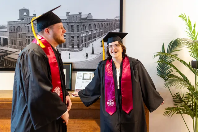 Two graduates laughing in bright window light.