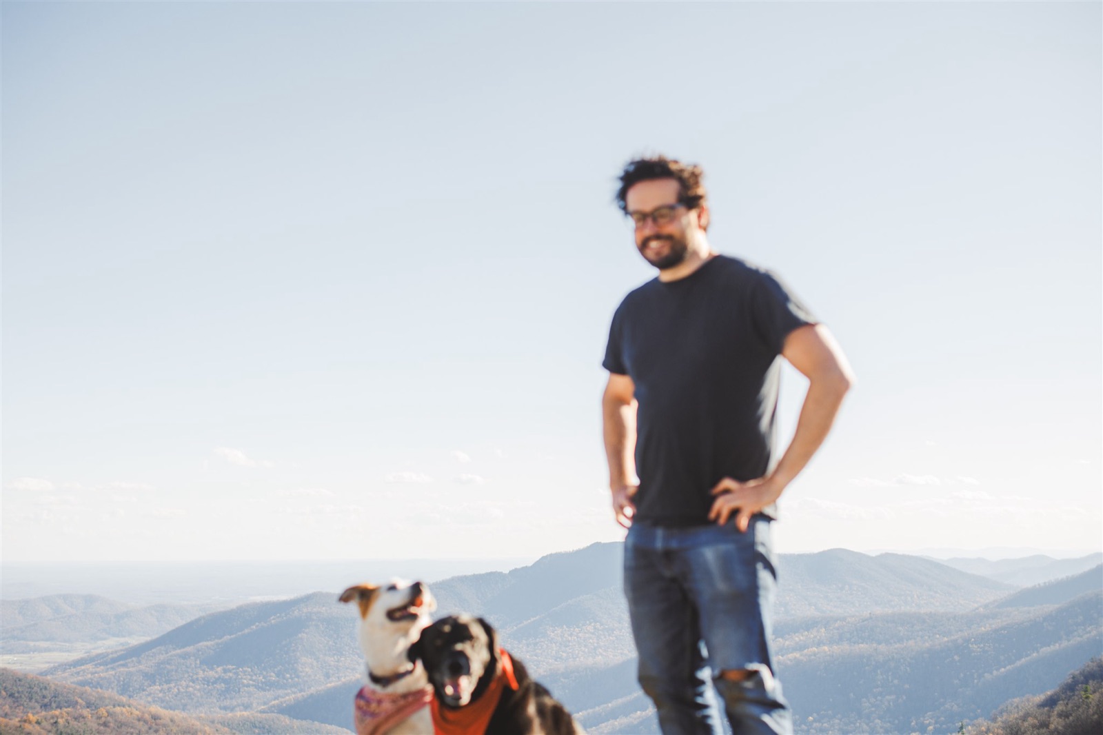 Aaron laughing on a Blue Ridge summit with Cal and Sugar looking up, hazy autumn ridgelines rolling away for miles behind them
