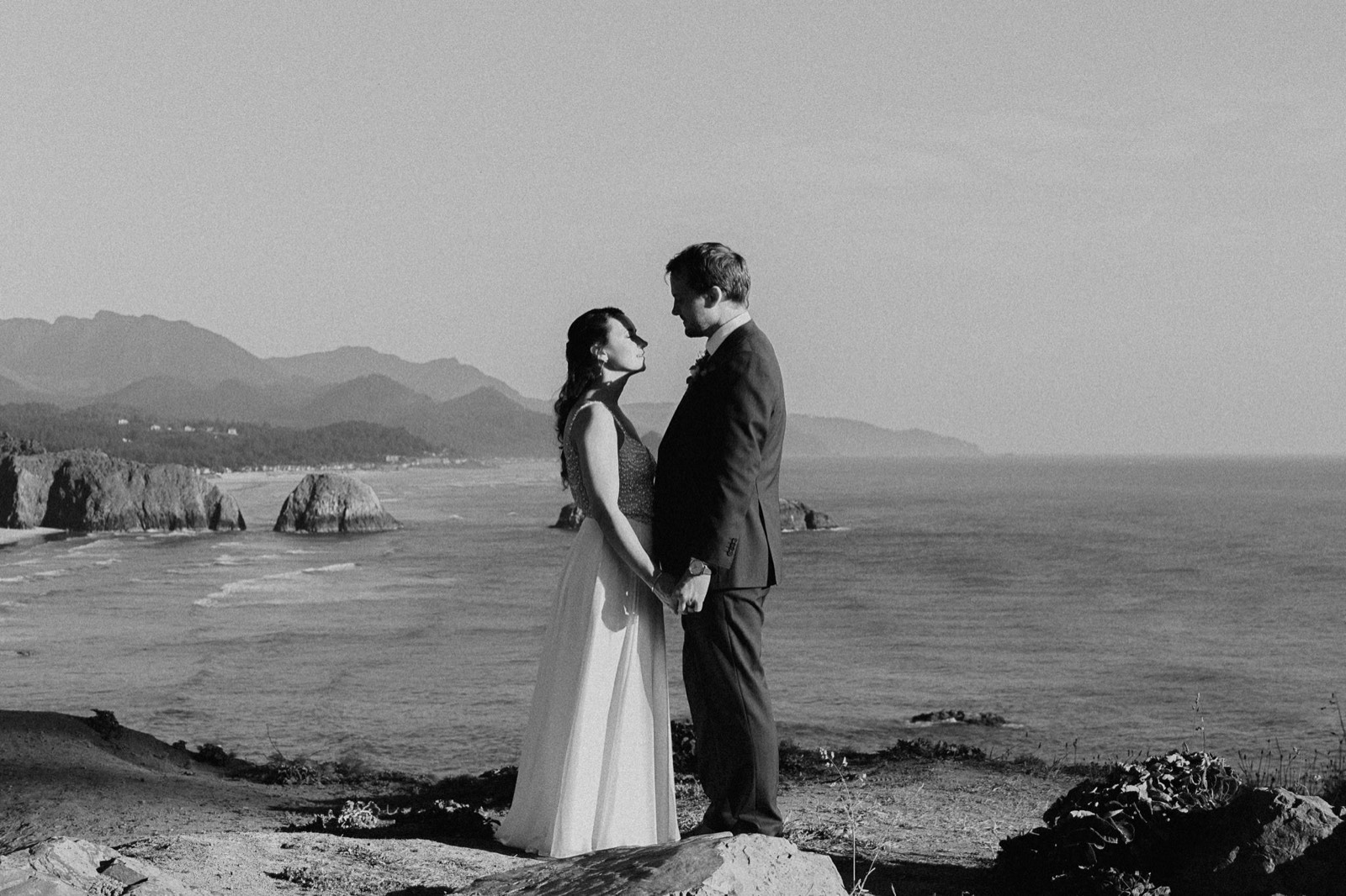 The couple on a cliff overlook above the Pacific, sea stacks and mountains behind them