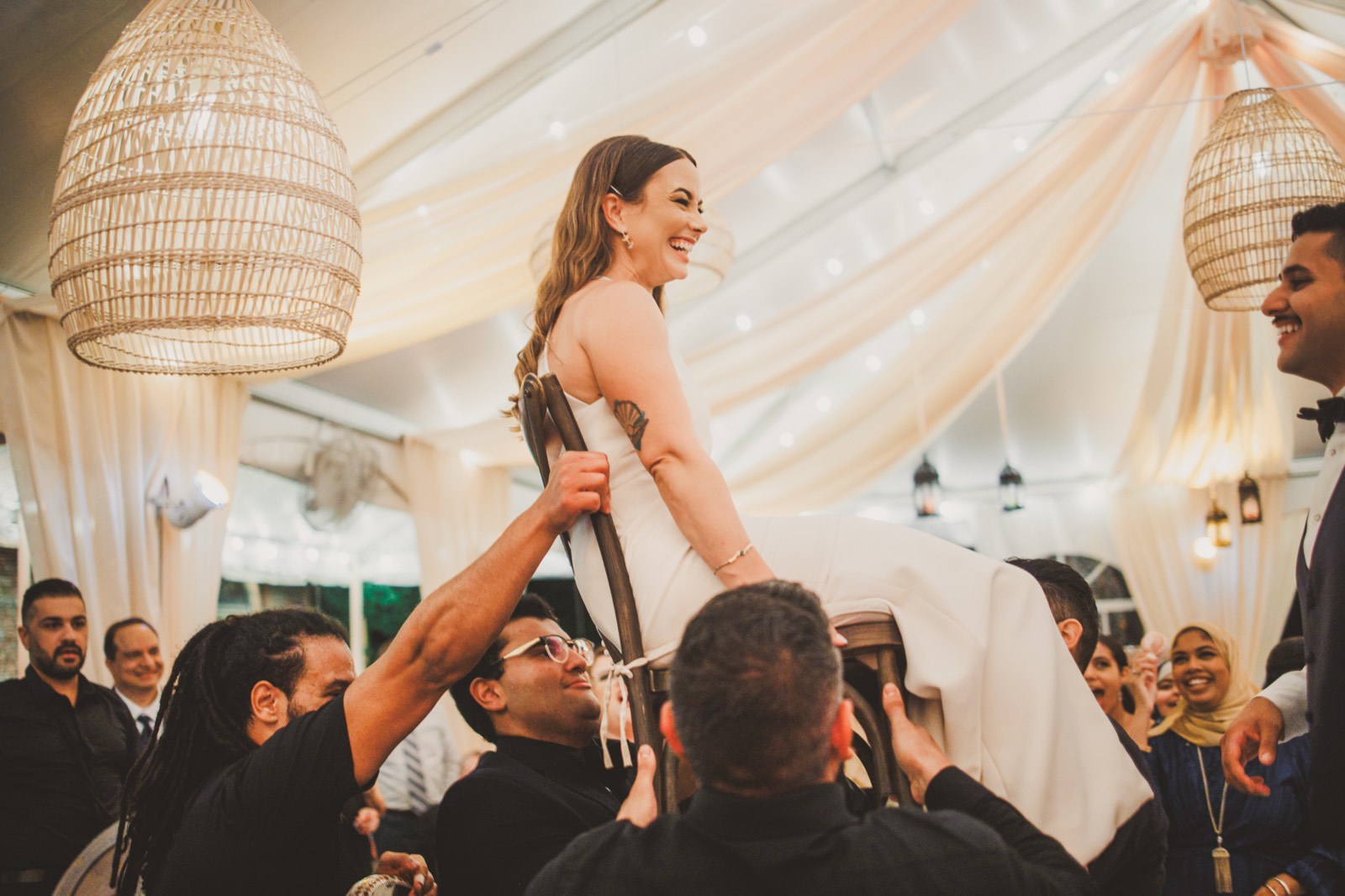 A drum circle lifting the couple on chairs, Zaffe-style, at their backyard reception tent