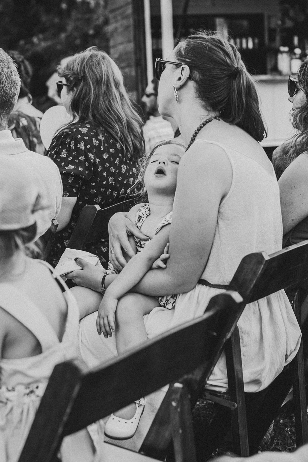 A toddler fast asleep on her mother's lap during the ceremony, black and white