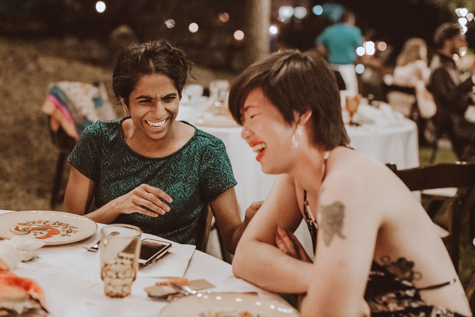 Two guests at an outdoor reception table laughing hard together over the place settings