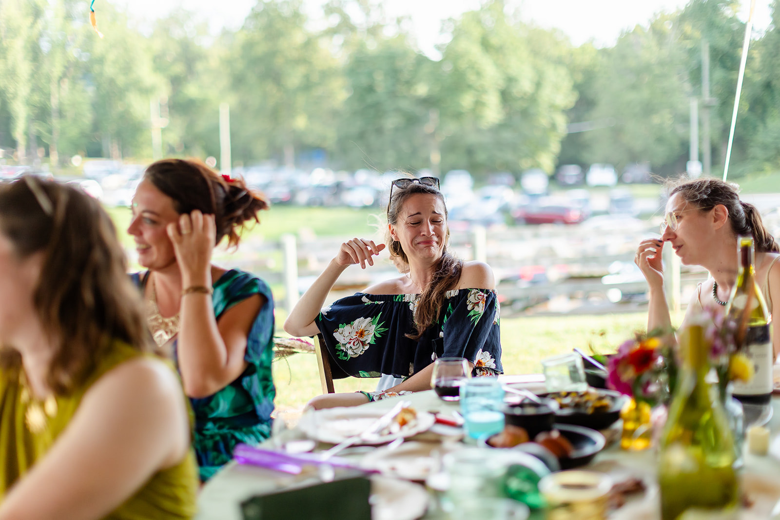 A guest scrunching her face in helpless laughter at an outdoor dinner table while friends crack up around her