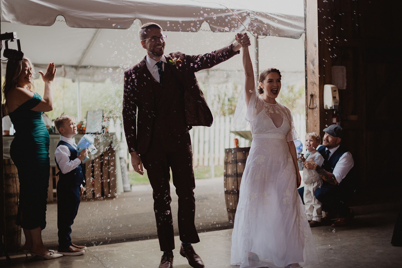 A bride and groom walk forward with their clasped hands raised through a shower of confetti as guests stand on both sides.