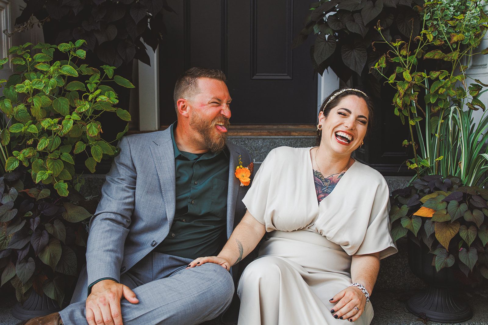 The couple sits together on stone front steps and the bride laughs with her head tipped back while the groom turns to watch her.