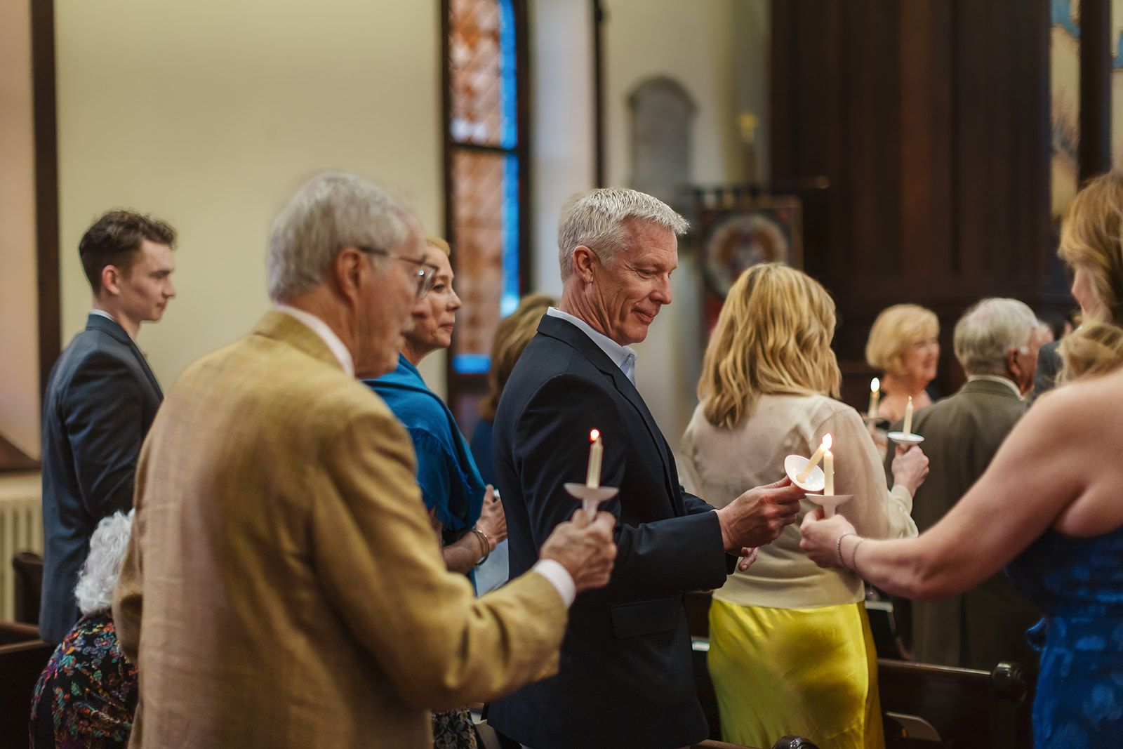 Guests standing in the pews of a church tip their lit taper candles toward one another to pass the flame along the row.