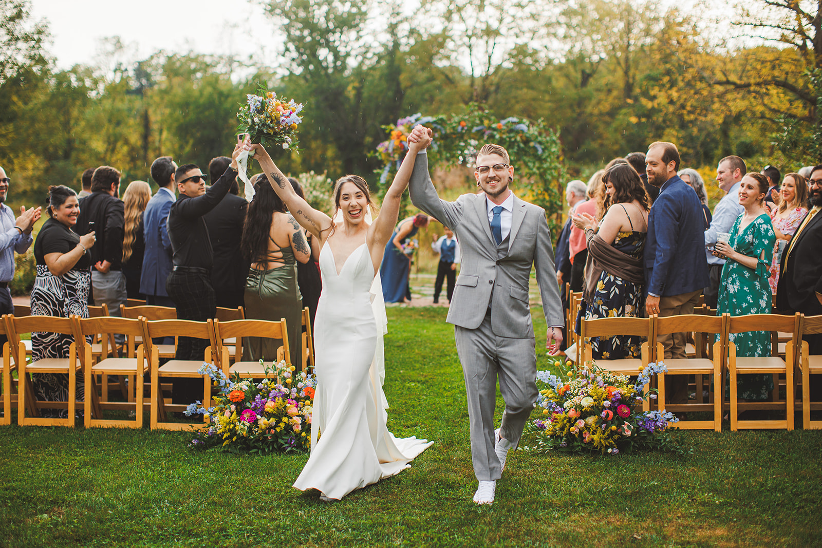 A couple raising their joined hands walking back up the aisle while guests cheer