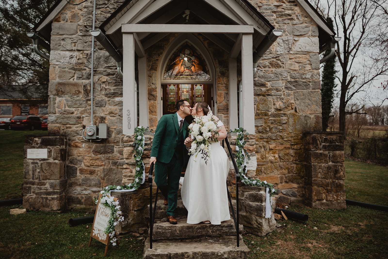 Mersades and Rogelio walking down the stone steps of their church after the ceremony, a greenery garland along the railing and bare winter trees behind