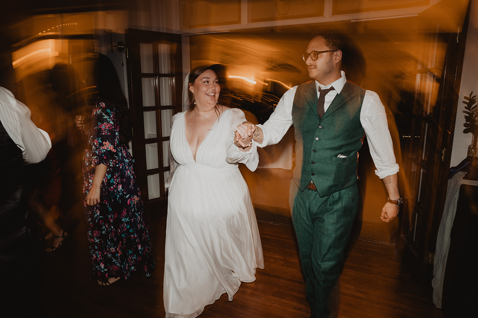 Mersades and Rogelio walking hand in hand into their reception, guests blurred with movement on either side