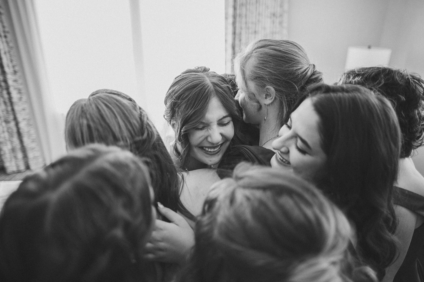 A black and white huddle of friends holding on to each other, faces pressed together, laughing