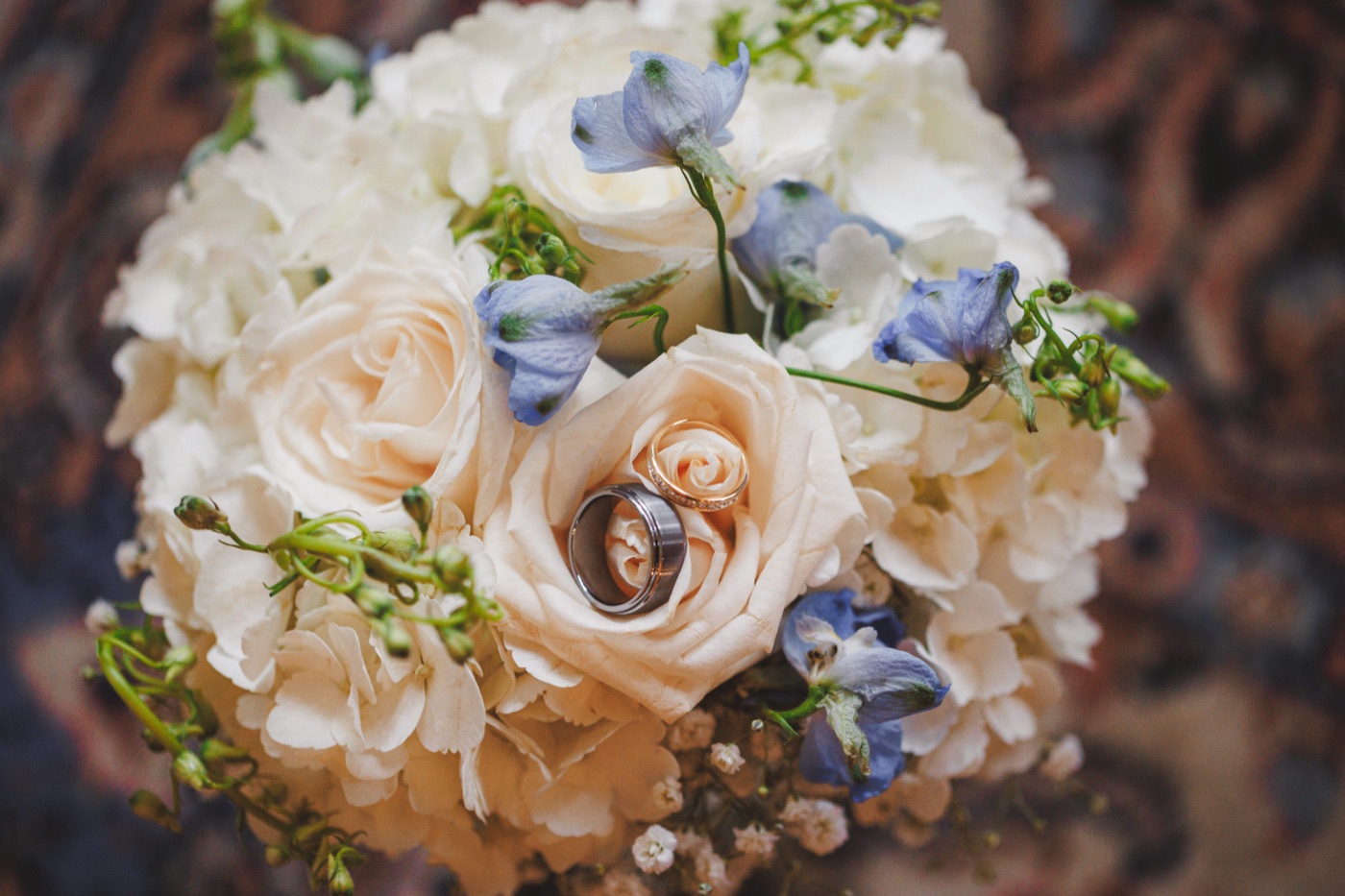 Two wedding bands nestled inside a blush rose at the centre of a white and blue bridal bouquet