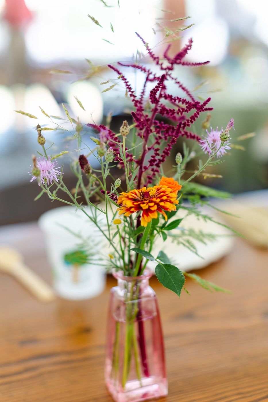 A single wildflower stem of zinnia, amaranth and grasses in a pink pressed-glass bud vase